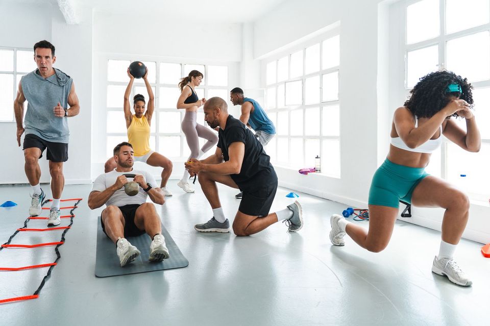 A bright group functional-fitness class with people doing lunges, core work and medicine-ball lifts