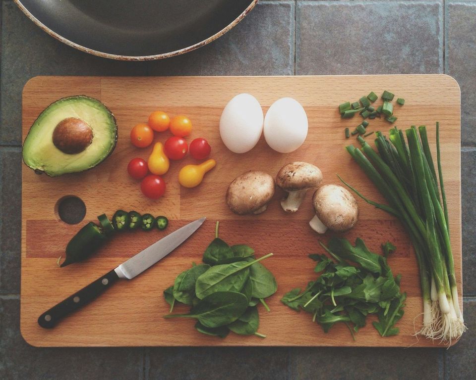 Fresh ingredients on a cutting board: avocado, tomatoes, eggs, mushrooms and greens