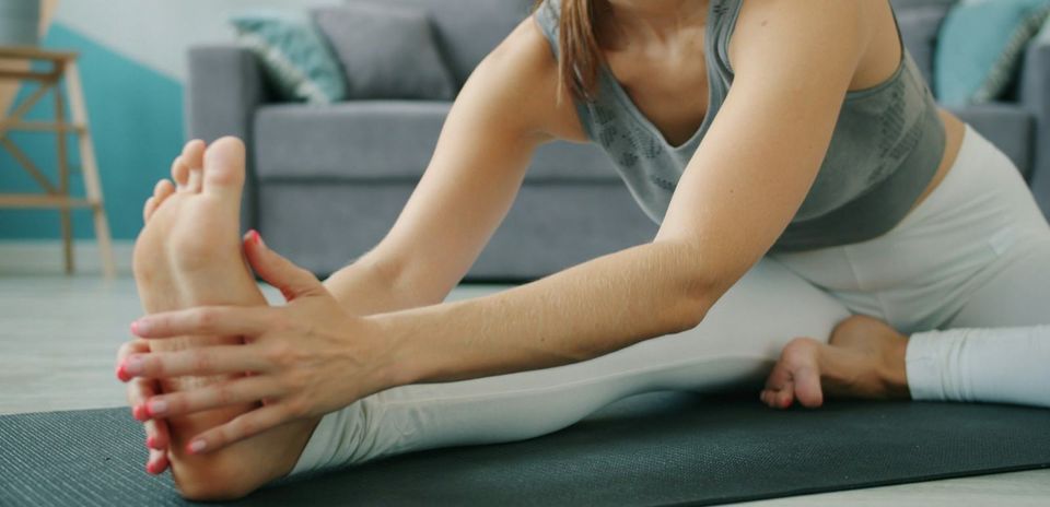A woman stretching her hamstrings on a mat at home