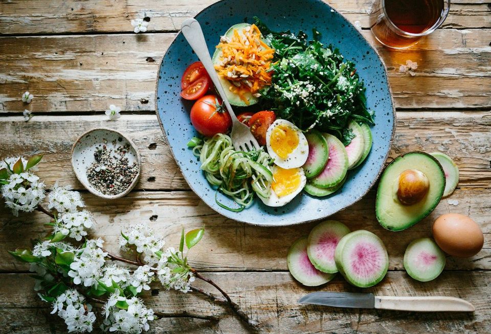 A plate of eggs, avocado and fresh vegetables on a wooden table